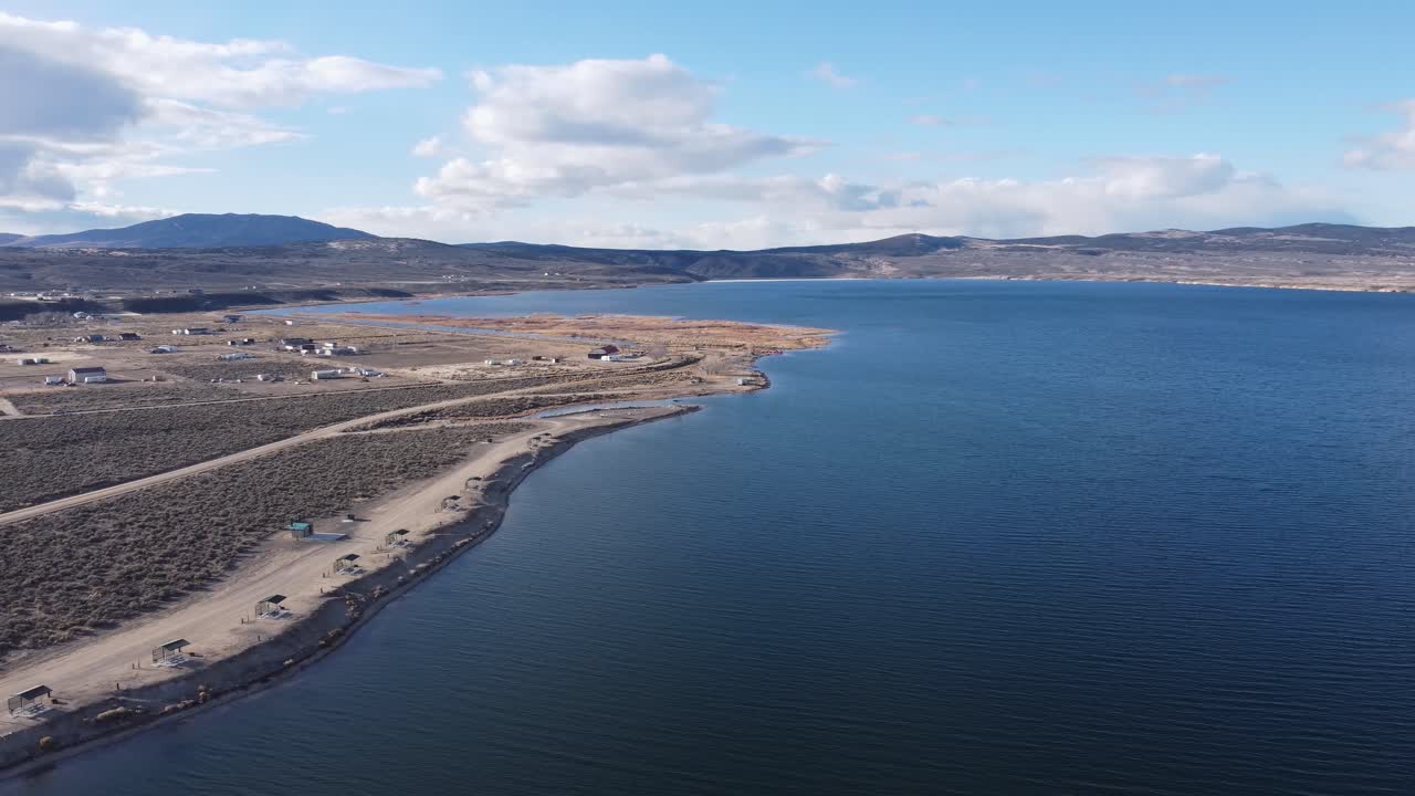 Aerial shot of desert landscape contrasted by clear blue water of the river or lake cutting through the Northern Nevada hills. Contrasted by dirt roads, fluffy clouds, and a rural landscape.