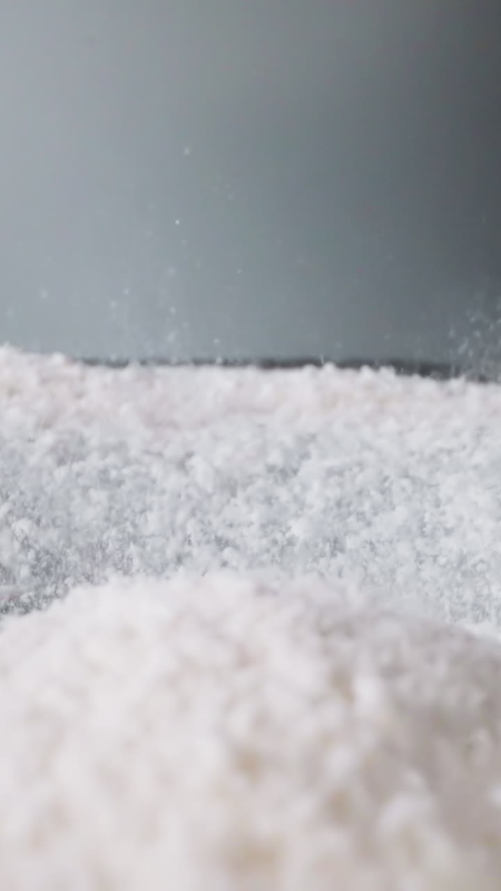 Pile of white starch bounces and spills into shaken vessel. Finely ground foodstuff moves up and down. Movement of powdered ingredient for cooking macro