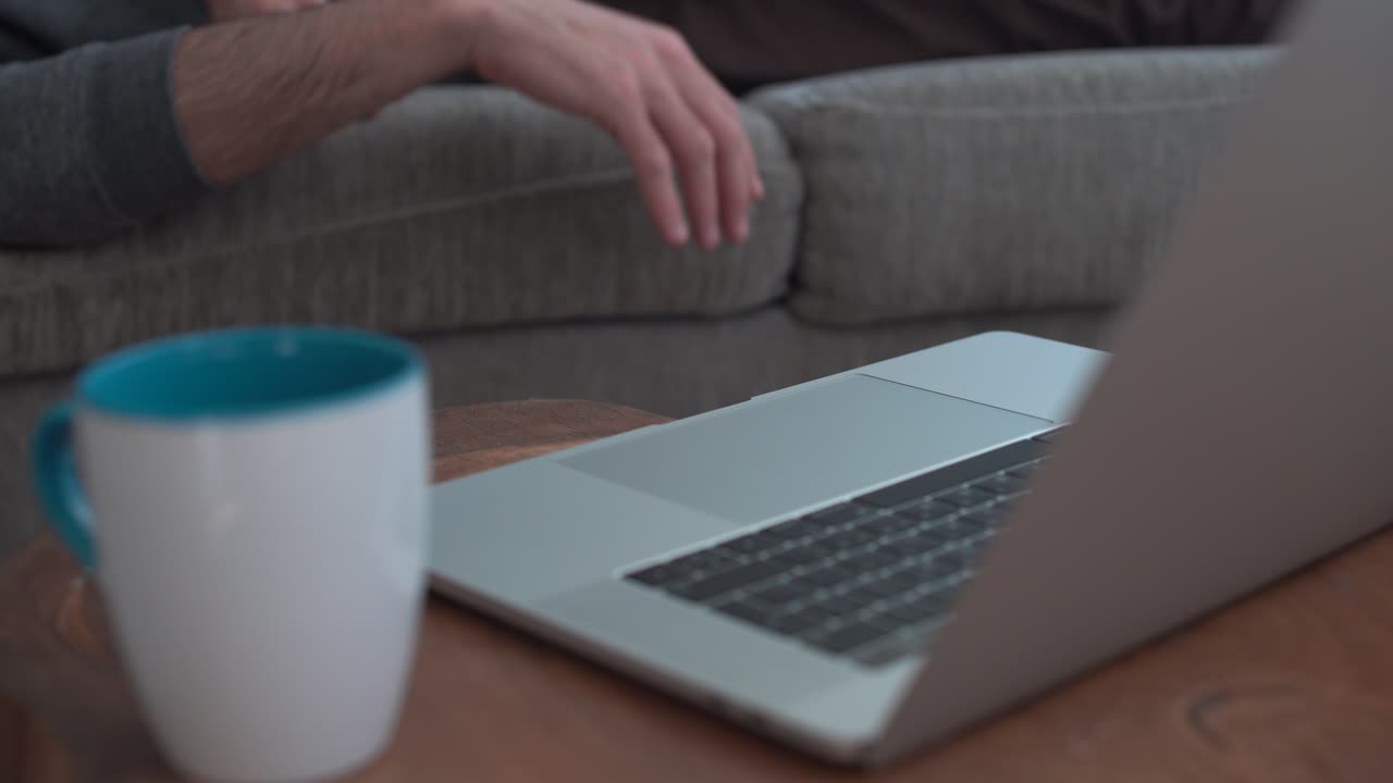 Lazy man lying on couch tries to reach the computer but can't make it