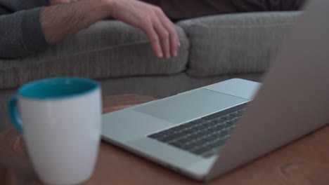 lazy man lying on couch tries to reach the computer but can't make it