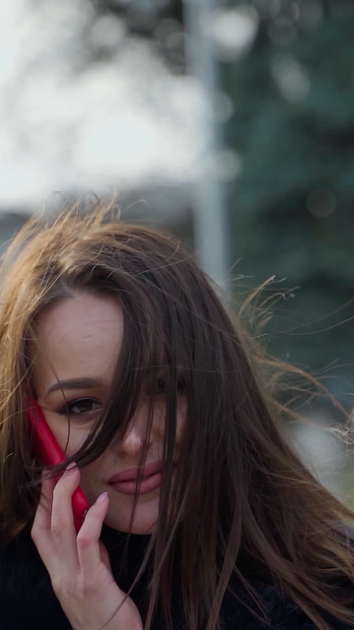 Portrait of a beautiful woman with long hair. Dark-haired lady talking on the phone and posing to camera on a city background. Slow motion. Vertical video