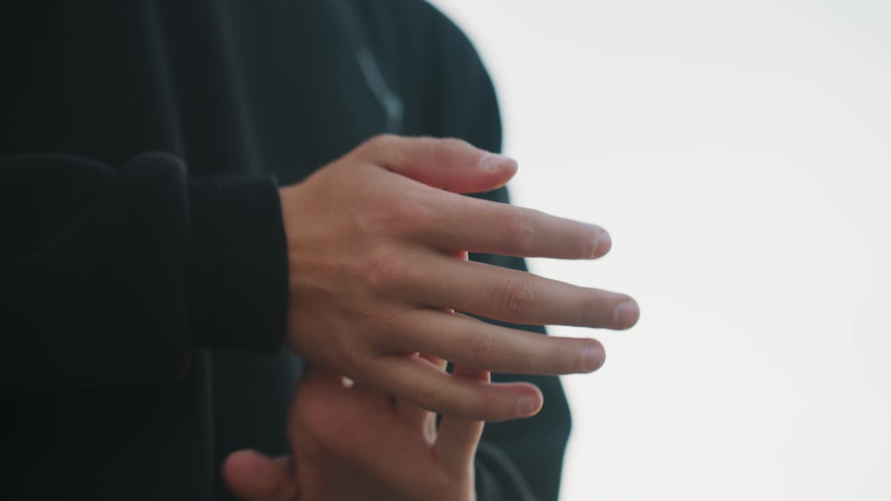 Mani minimaliste, movimenti delicati delle dita, una persona con un maglione scuro pratica allungamenti aggraziati e ispezione delle unghie contro uno sfondo luminoso e ad alta chiave, gesti lenti e controllati evocano calma e concentrazione.