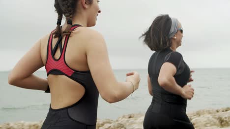 amigas atléticas positivas trotando a lo largo del paseo marítimo