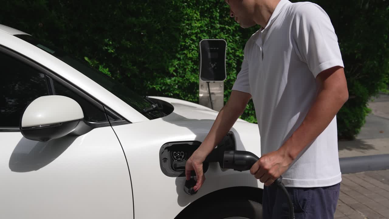 Ev şarj istasyonundan elektrikli aracına (EV) şarj kablosunu takan ilerici adam.