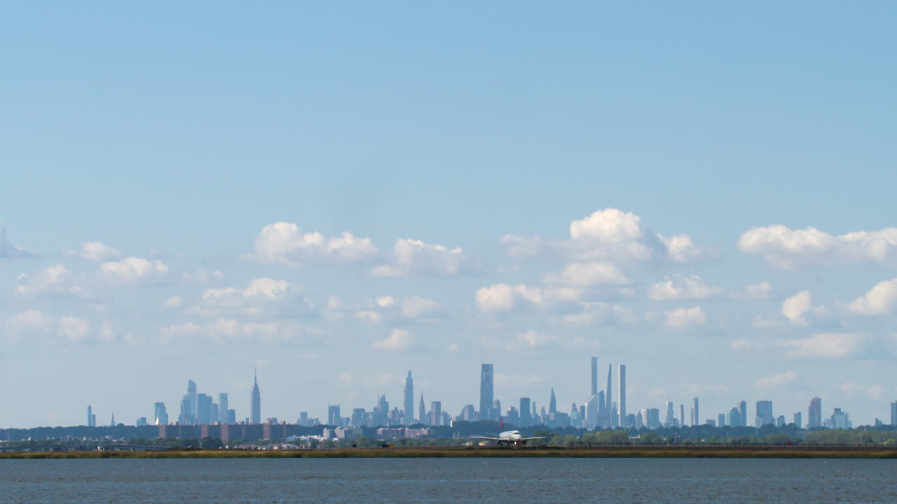 Commercial Jet Crosses Frame Against Clear Blue Sky as Camera Tilts Down to New York City Skyline on Horizon