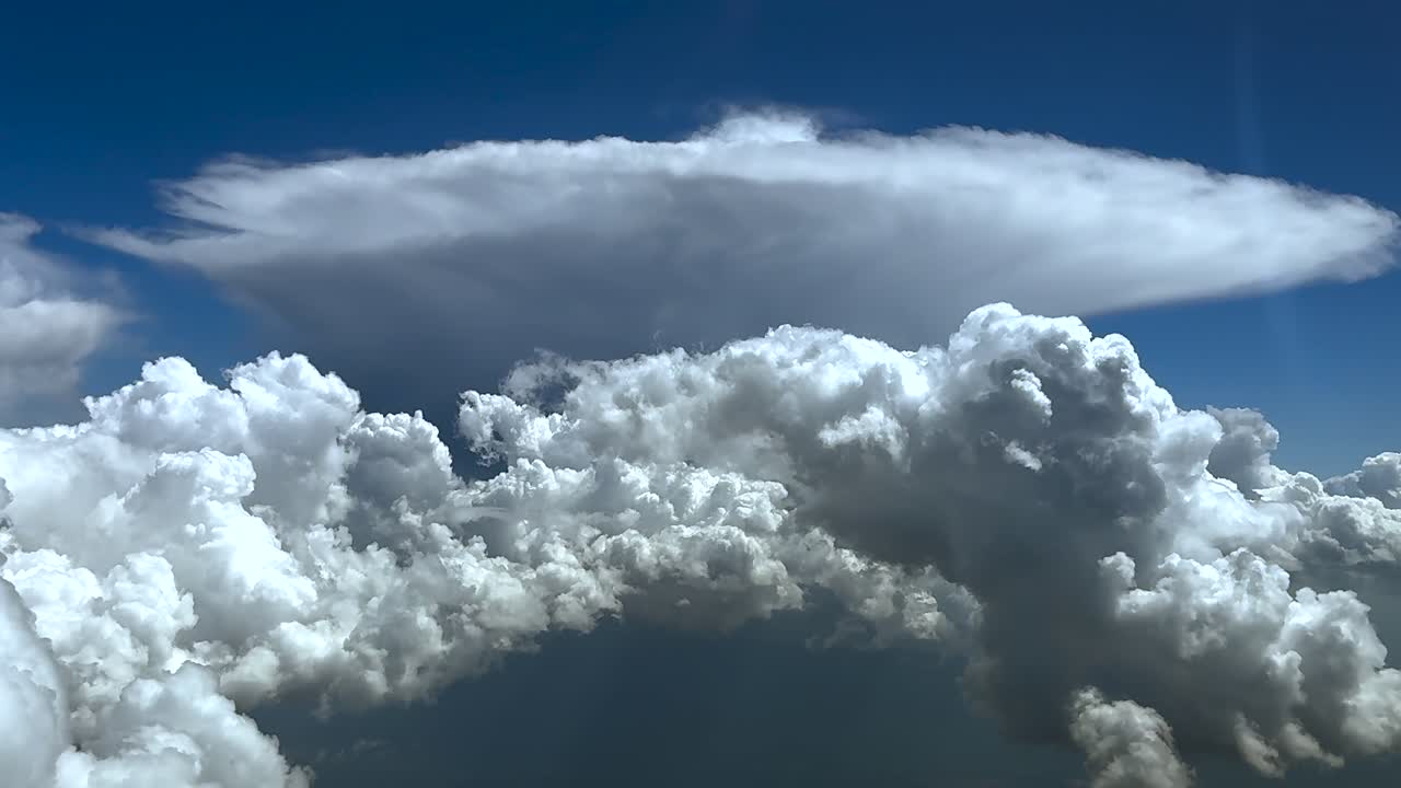 Flying through storm clouds, as seen by the pilot from a jet cockpit, with a huge cumulonimbus cloud with a perfect anvil shape, under an intense blue color sky. Ultra-realistic 4K.