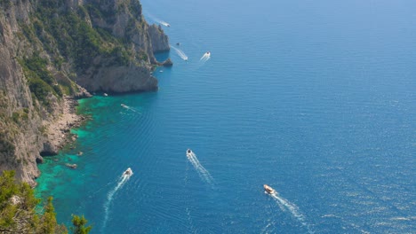 High-angle-cinematic-shot-over-motor-boats-sailing-around-in-crystal-blue-waters-of-Tyrrhenian-sea,-Capri-Island,-Italy-at-daytime