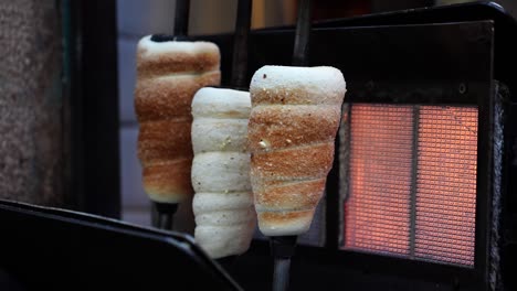 Chimney-cake-preparation-process-near-heated-electric-wall-in-outdoor-bakery