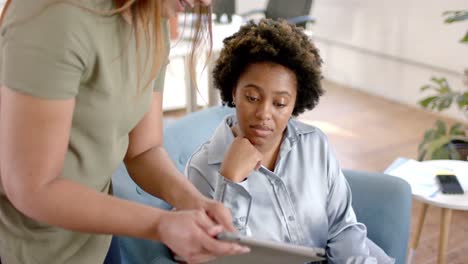 diverse business female colleagues in discussion using tablet in casual office meeting, slow motion