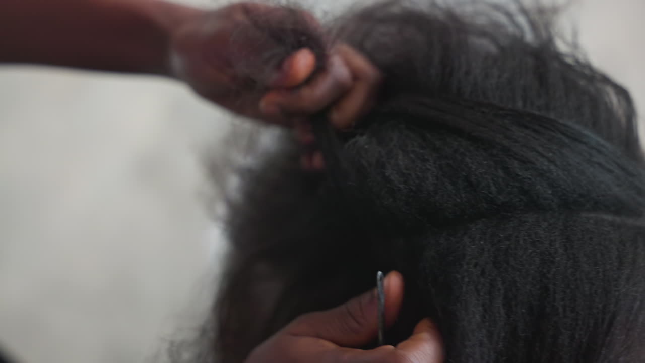 Primo piano di mani che districano capelli naturali, sequenza delicata a casa che mostra dita pazienti che separano i nodi usando pettine ed elastico per lisciare un afro testurizzato, luce soffusa e calda atmosfera domestica, messa a fuoco