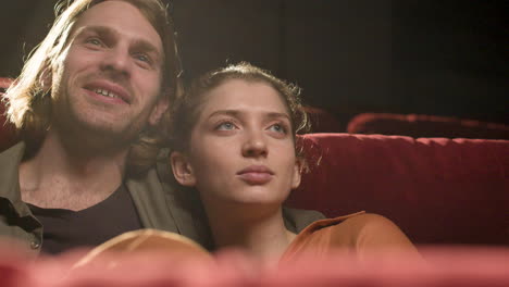 vista de cerca de una pareja sentada en el cine viendo una película y sonriendo