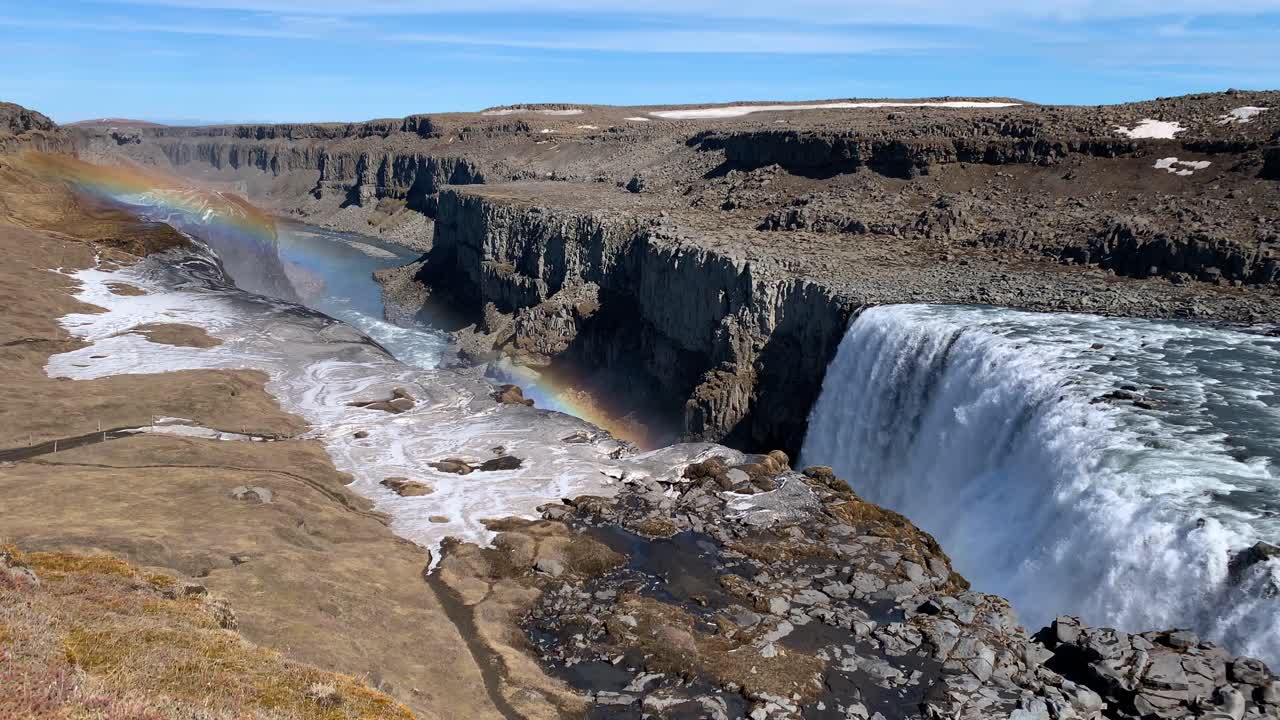 The dry and rocky Icelandic landscape around Dettifoss, wich is one of the most powerful waterfalls in Europe, on a sunny day with a beautiful rainbow appearing in the sky