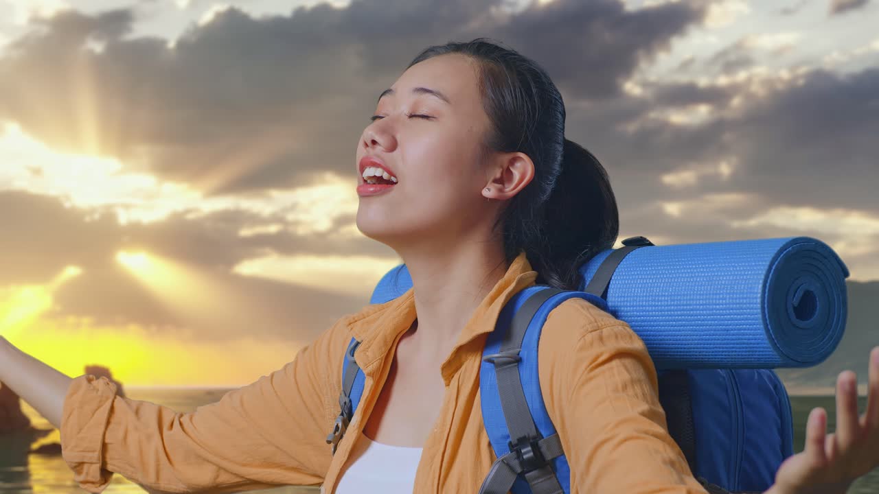 Close Up Side View Of Asian Female Hiker With Mountaineering Backpack Spreading Arms Enjoy Looking The View Around While Standing on Beach During Sunset Time