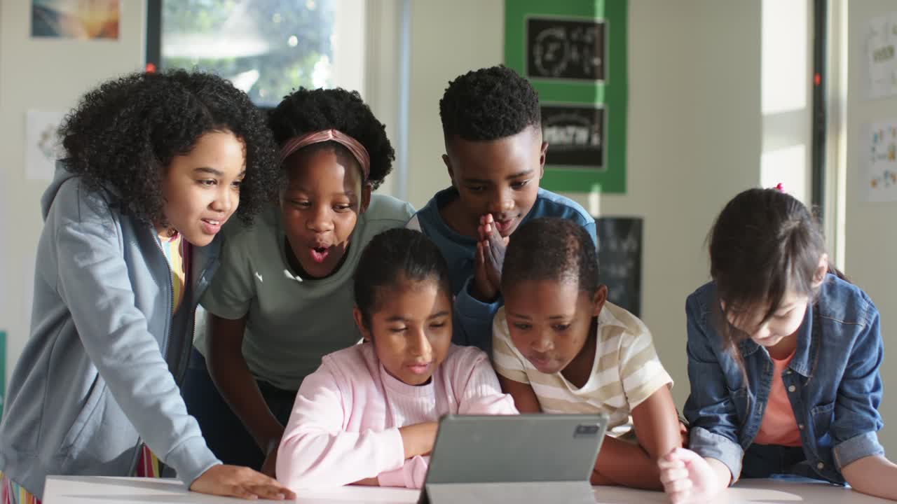Diverse classmates leaning around tablet on low table at school, watching content and collaborating