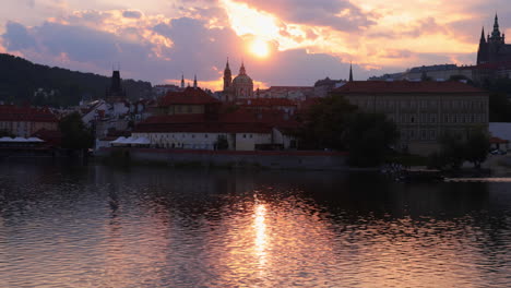 move past tree branches to reveal st nicholas church and vltava river at sunset_czech republic