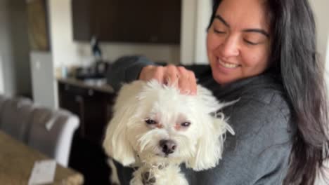 Young-woman-holds-cute-Maltese-dog,-petting-him-and-smiling