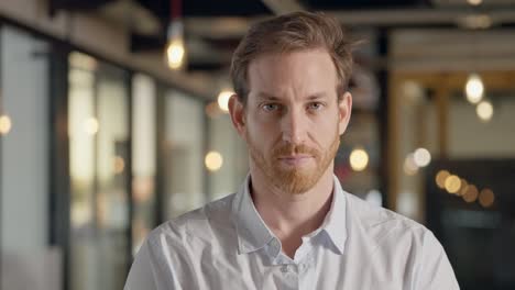 white caucasian man with blue eyes staring directly into camera with strong intense gaze, and confidence. portrait of businessman with mysterious and intrigue look standing in modern office with bokeh