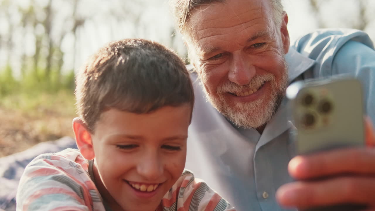 Grandfather and Grandson Smiling While Looking at Smartphone Outdoors