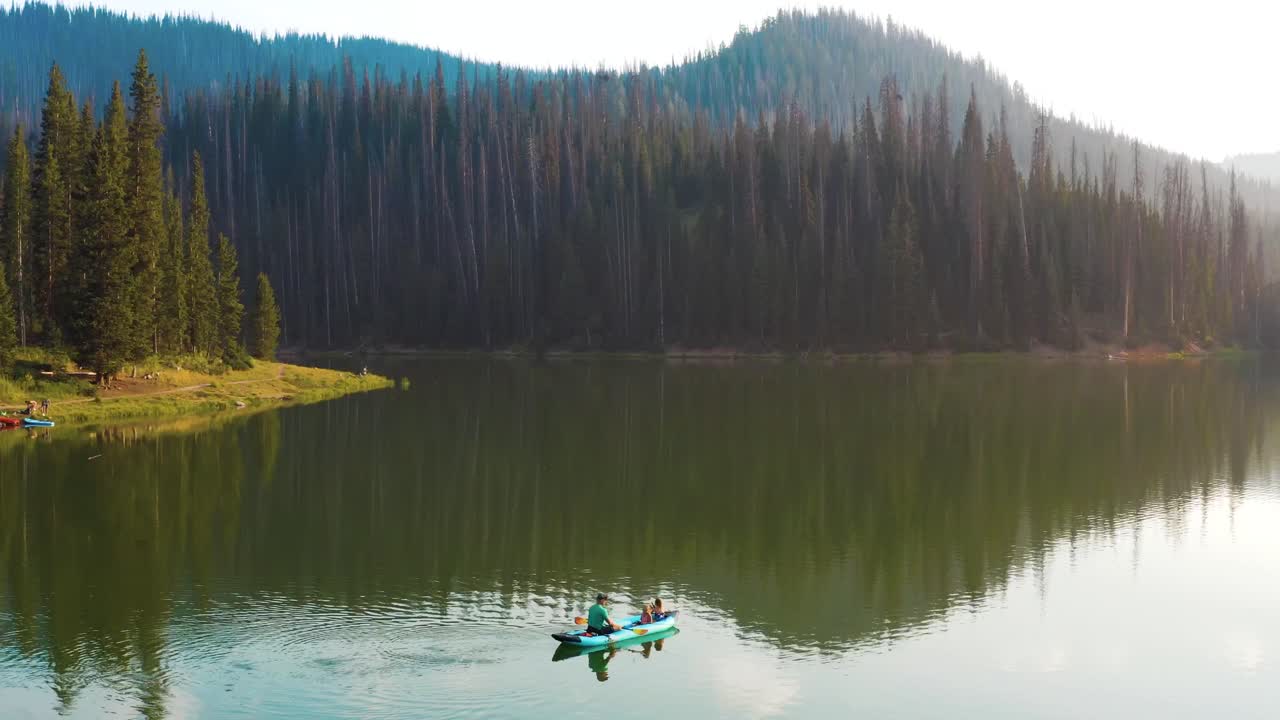 Luftaufnahme eines Mannes und seiner zwei Töchter beim Angeln in einem Kanu auf einem Bergsee während der goldenen Stunde