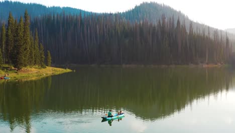 Toma-Aérea-De-Un-Hombre-Y-Sus-Dos-Hijas-Pescando-En-Una-Canoa-En-Un-Lago-De-Montaña-Durante-La-Hora-Dorada