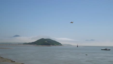 Barco-De-Pescadores-En-El-Mar-Amarillo-En-Marea-Baja,-Boya-De-Navegación-Roja-Flotando-Entre-Islas,-Una-Montaña-Cubierta-De-Niebla-Densa,-Isla-De-Ganghwado,-Corea-Del-Sur,-Ancho-Estático