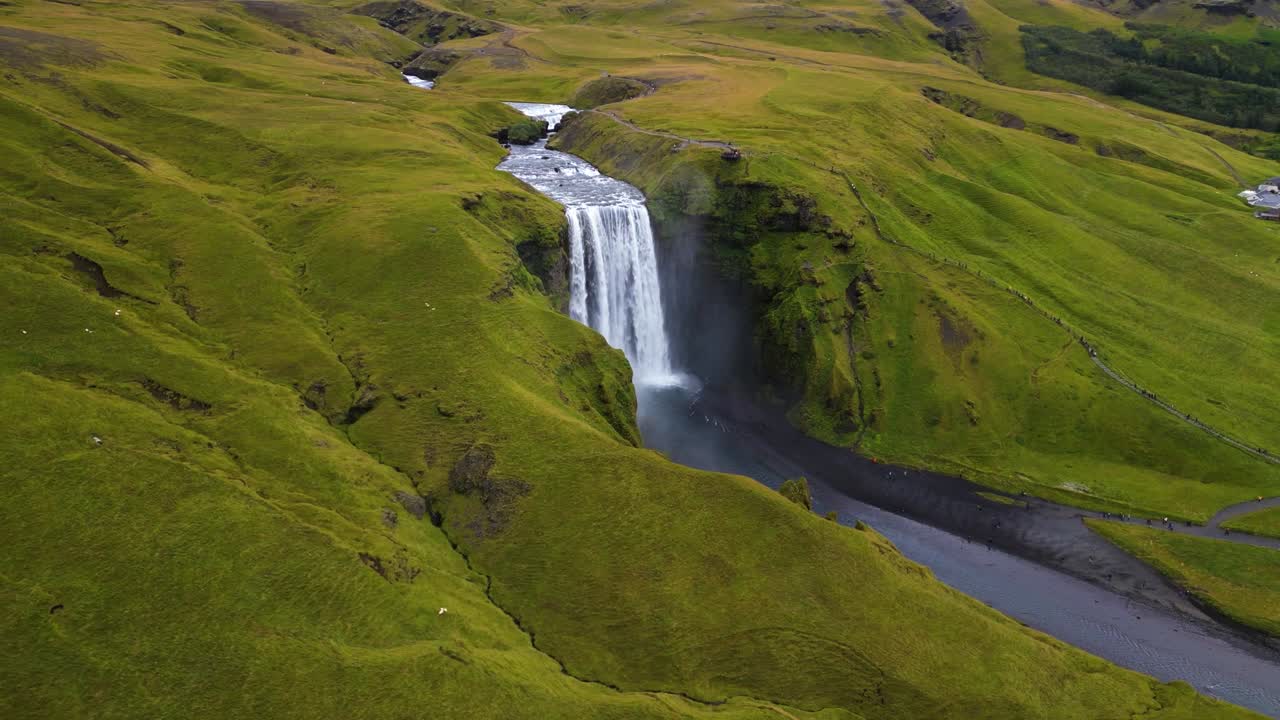 4K cinematic drone footage of Skógafoss Waterfall in Iceland, capturing the immense curtain of water cascading from towering cliffs surrounded by lush green landscapes. Iceland_29