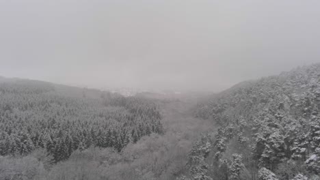 Heavy-winter-fog-covers-a-snow-laden-mountain-valley,-aerial-dolly