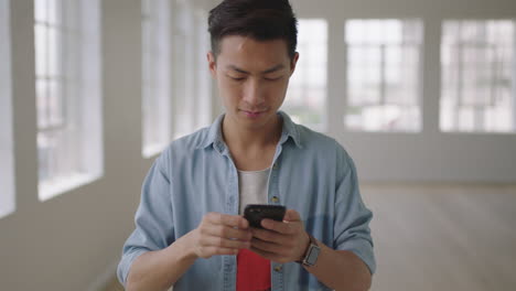 portrait of young asian man student texting browsing social media using smartphone mobile technology in empty apartment room