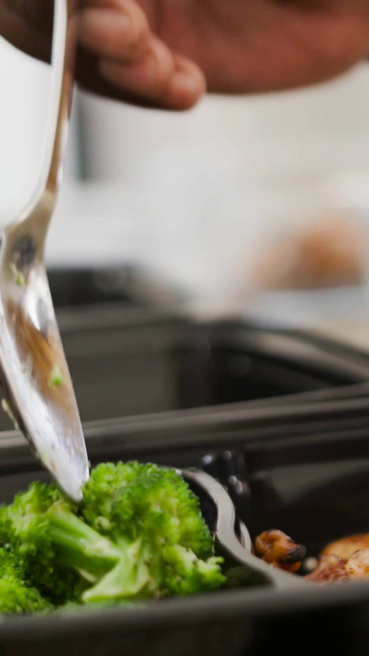 Video verticale: Mano che mette broccoli in un vassoio nero sul bancone con un cucchiaio per la preparazione