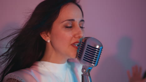 side view of a singer passionately singing into a vintage microphone, with her hair flowing against a blurred pink background