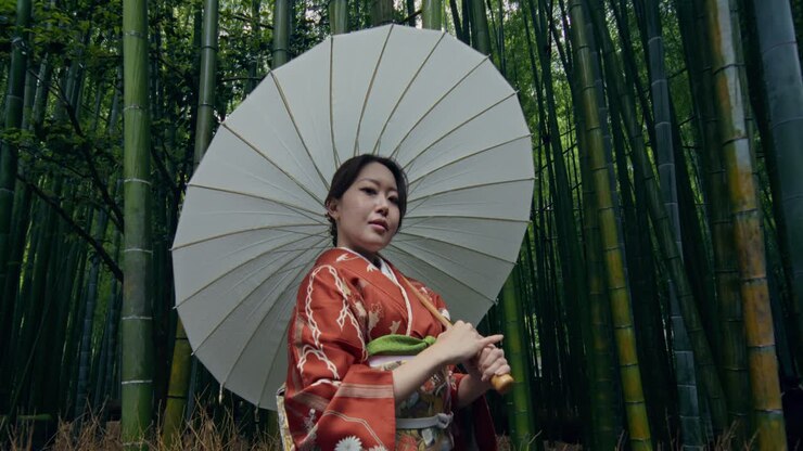 Donna in Kimono sotto un ombrello bianco in una foresta di bambù.