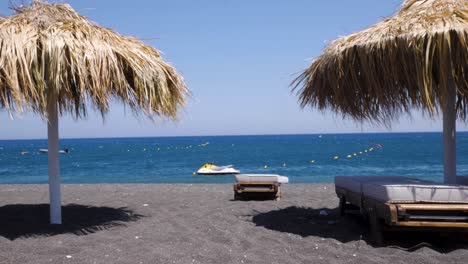 handheld moving wide shot of perissa beach in santorini greece, with black lava sand on a windy and sunny summer day