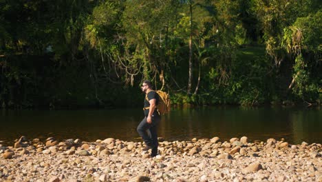 un joven viajero pasa por un arroyo de montaña en el bosque caminando sobre piedras en cámara lenta