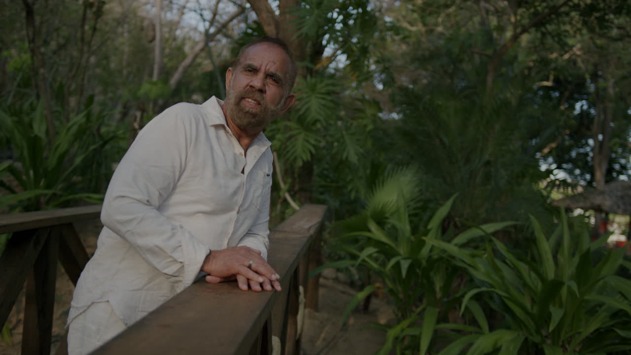 un hombre se apoya en una barandilla de madera y sonríe, perdido en sus pensamientos mientras se pone el sol