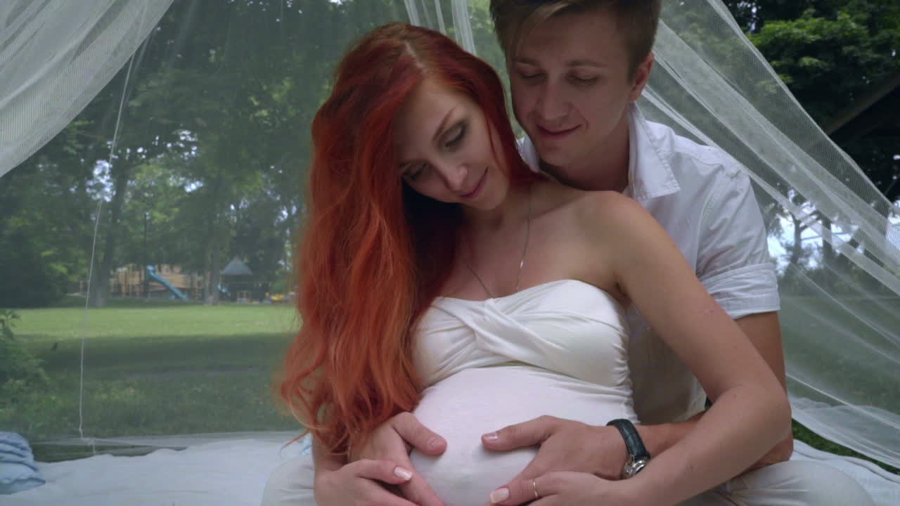 Man hugging pregnant woman in romantic decorations at park. Love couple