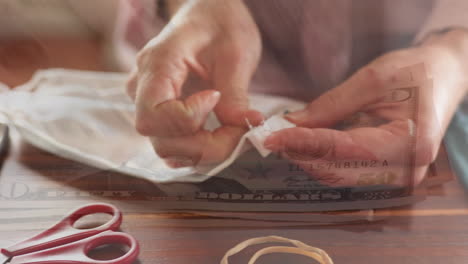 digital composite video of american dollar bills moving against woman sewing face masks