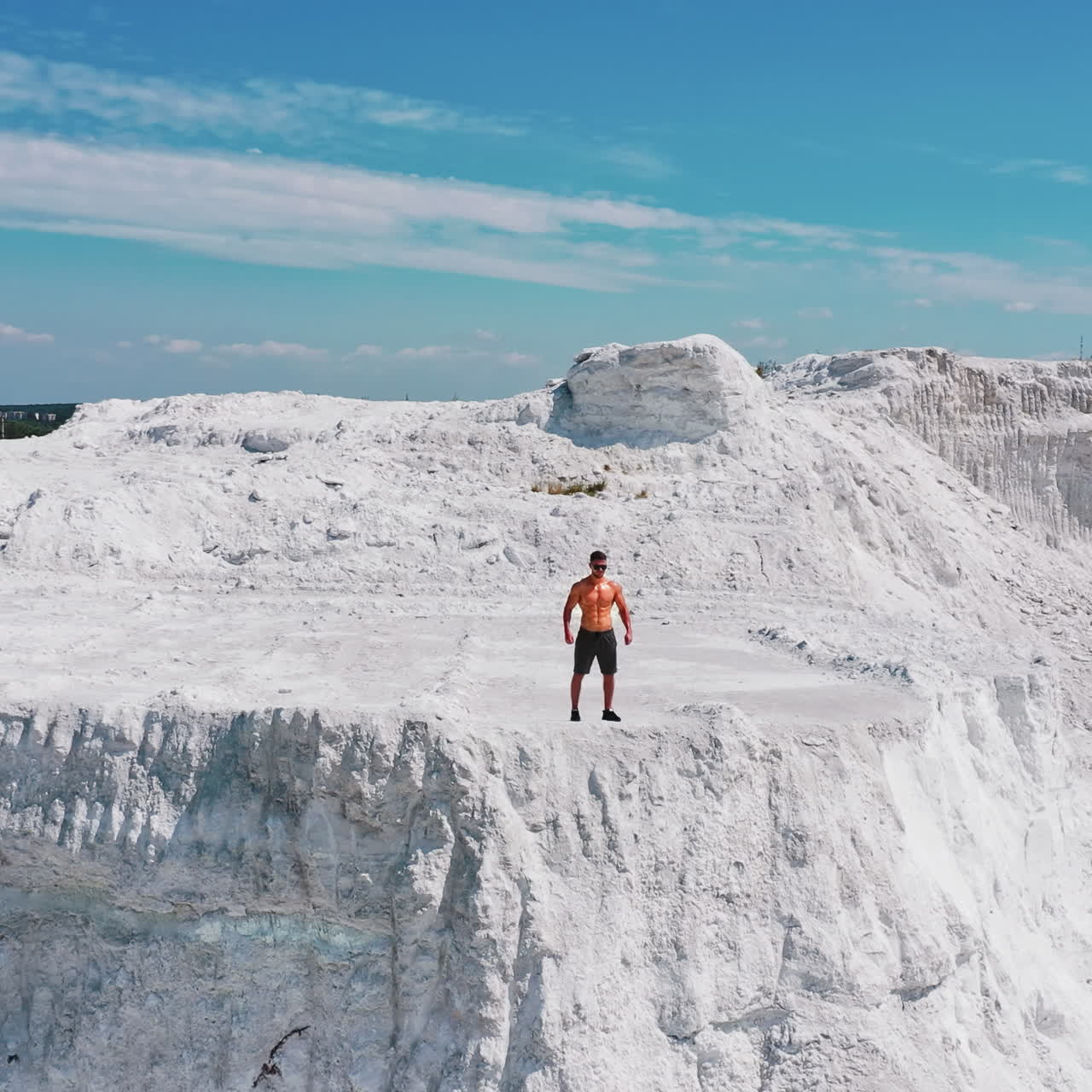 Muscular bodybuilder running on white rocky canyon. Shirtless man of fitness body doing his workout in the mountains in a warm sunny day. Camera moves back.