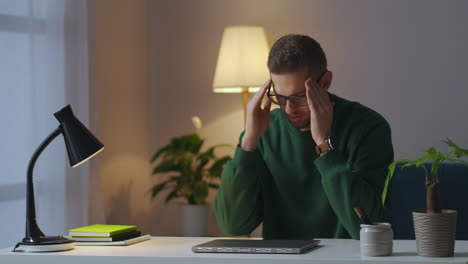 hombre sobrecargado de trabajo en casa por la noche cerrando la computadora portátil y frotándose los ojos y la cara quitando las gafas trabajo remoto y independiente