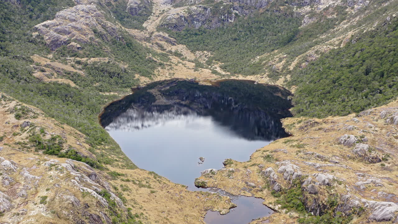 Highland lake and rugged rocky landscape seen from above along Beagle Channel trail, reflection of mountains in water