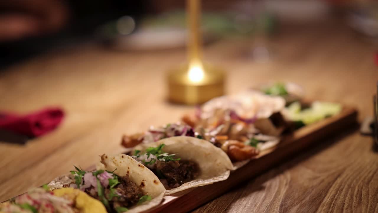 A variety of tacos arranged on a wooden table, illuminated by warm candlelight, creating a cozy dining atmosphere