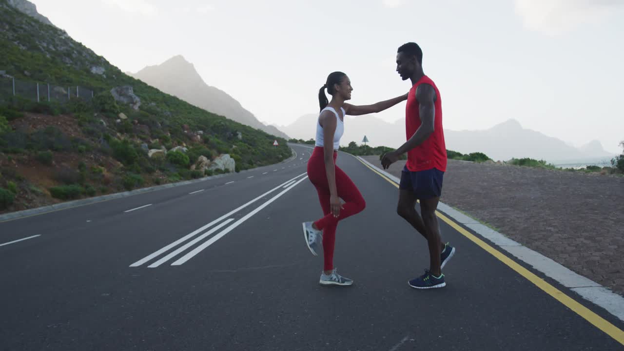 Diverse fit couple exercising stretching on a country road near mountains