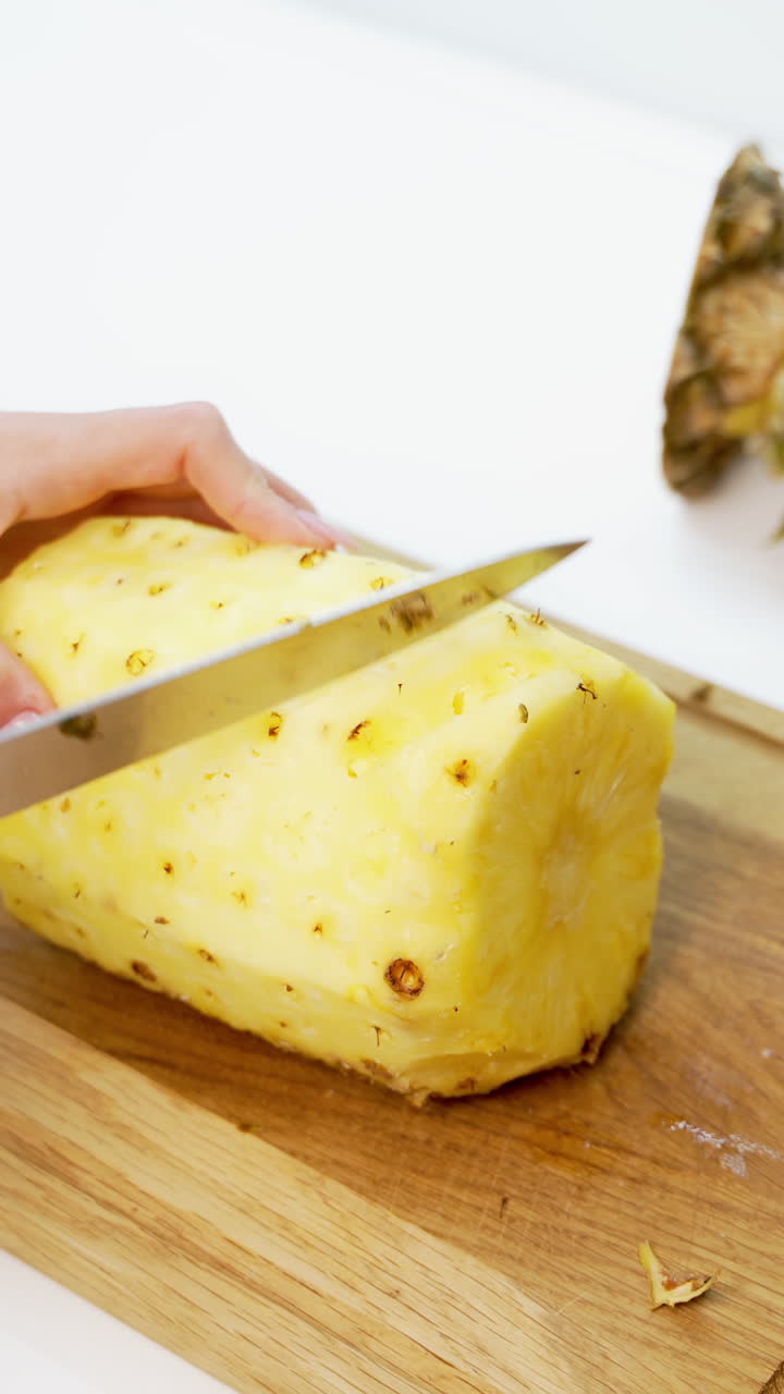Fresh peeled pineapple on a wooden board. Woman's hands holding sharp knife and cleaning pineapple on the table. Vertical video