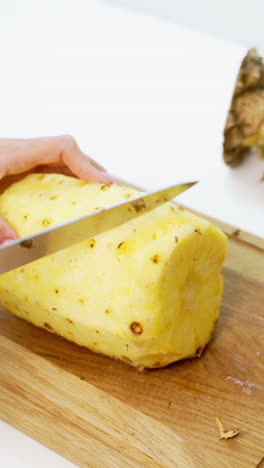 fresh peeled pineapple on a wooden board. woman's hands holding sharp knife and cleaning pineapple on the table. vertical video