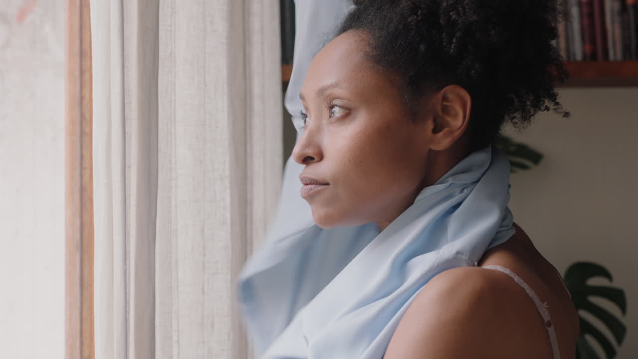 bella donna afroamericana che si veste, si prepara tardi per il lavoro, guarda fuori dalla finestra, si gode il nuovo giorno, si sente riposata.