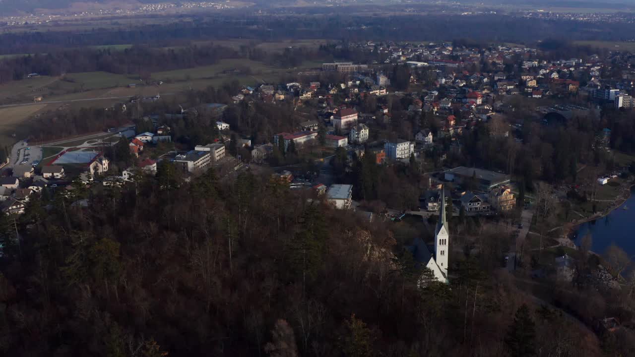 vista aérea inclinada hacia abajo sobre la ciudad de bled y la iglesia frente al lago con montañas en el fondo en eslovenia