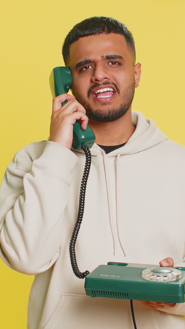 Tired bored man talking on wired vintage telephone exhausted of talk making silly faces fooling