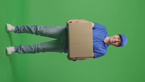 full body of asian male courier in blue uniform smiling while delivering a carton on green screen background in the studio