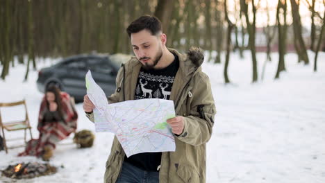 caucasian man checking map for directions in a snowed forest.