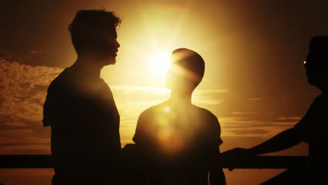 A-group-of-friends-have-a-discussion-on-the-beach,-silhouetted-by-the-sunset-in-the-background