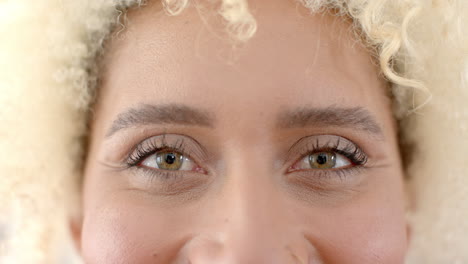 close-up of a young biracial woman''s eyes, framed by curly blonde hair, at home